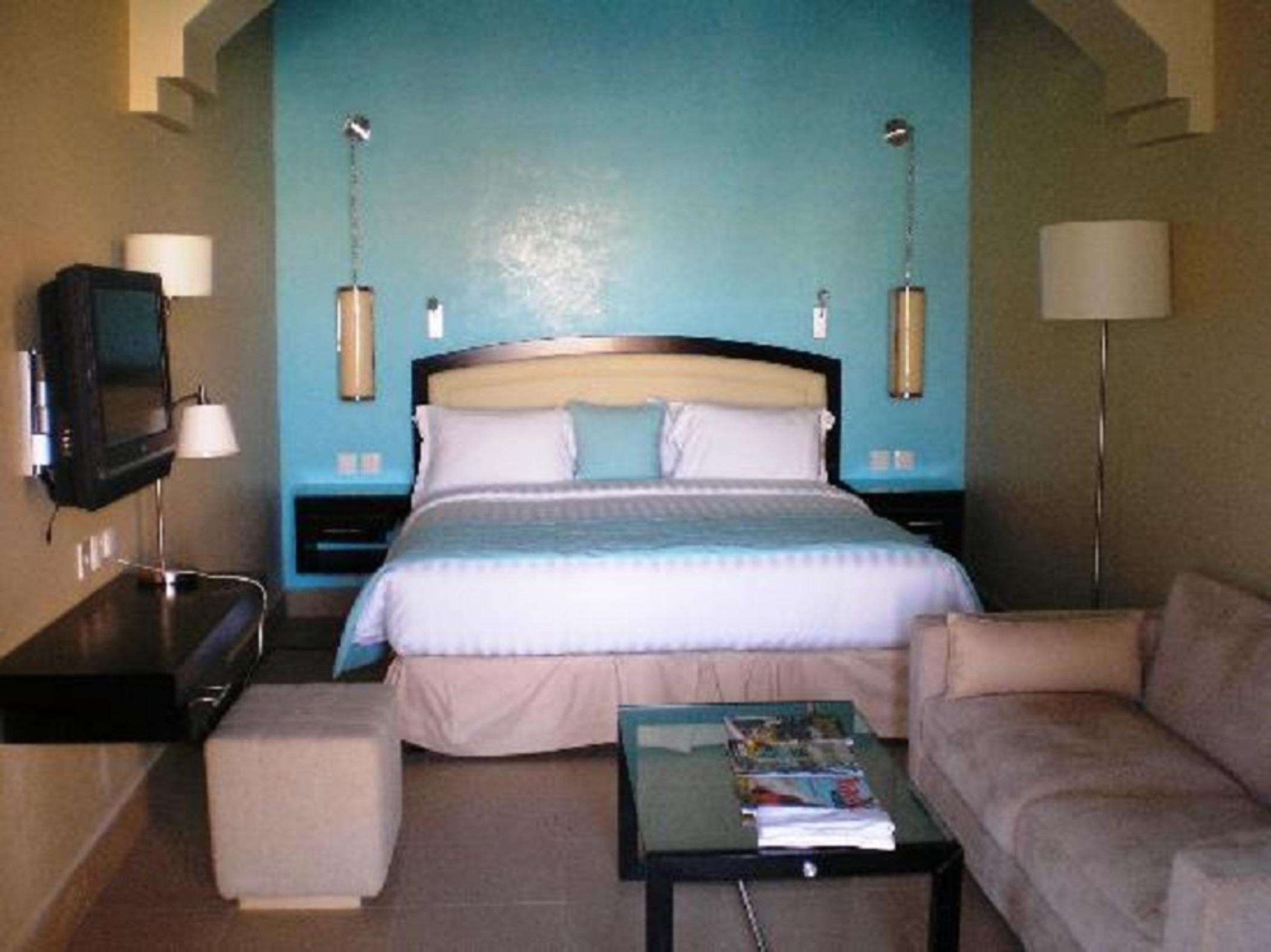 The Cove Rotana Resort - Ras Al Khaimah Kültér fotó The photo shows a modern hotel room with a stylish design. It features a large bed with white linens and a light blue accent, against a backdrop of a blue wall. On either side of the bed are wall-mounted lamps. There is a flat-screen TV mounted on th